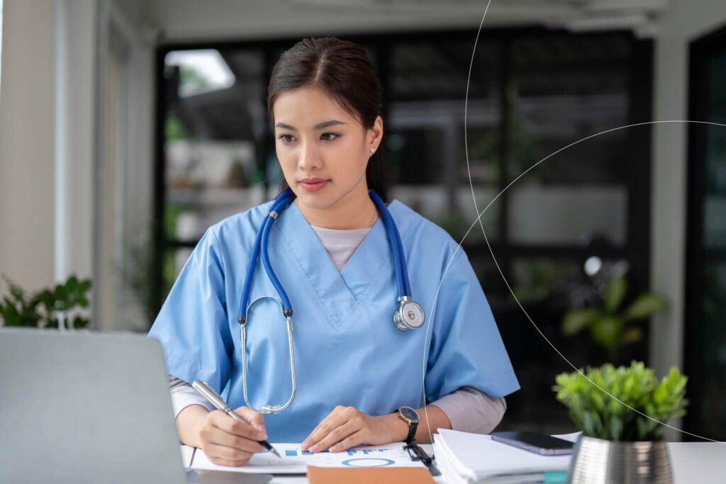 A female nurse in blue scrubs reviewing cardiovascular research on heart failure at her computer desk.