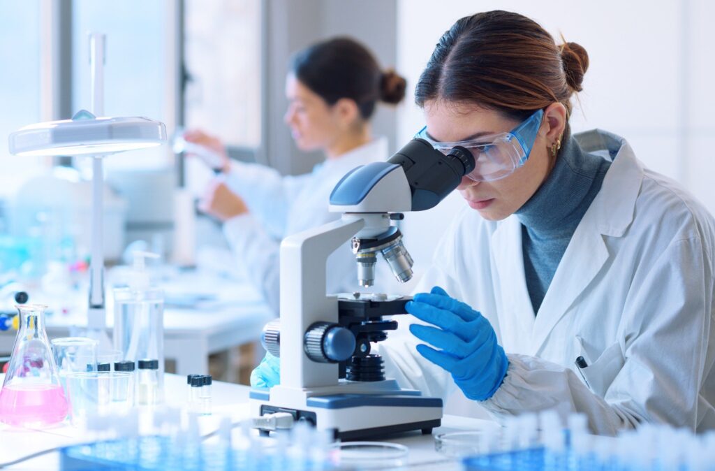Scientist examining samples under a microscope during early-phase clinical research.